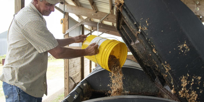 A man dumps food scraps from a bucket into a larger composter. 
