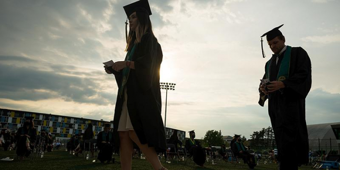 Two graduates walk across the stage at University of Vermont Commencement ceremony