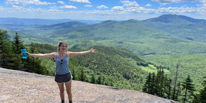 Deniz Dutton standing on a hiking trail with a green mountainous view behind her