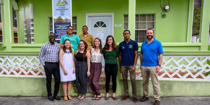 group of students, faculty and partners standing in front of a green building that has a sign reading "PItons Management Area"