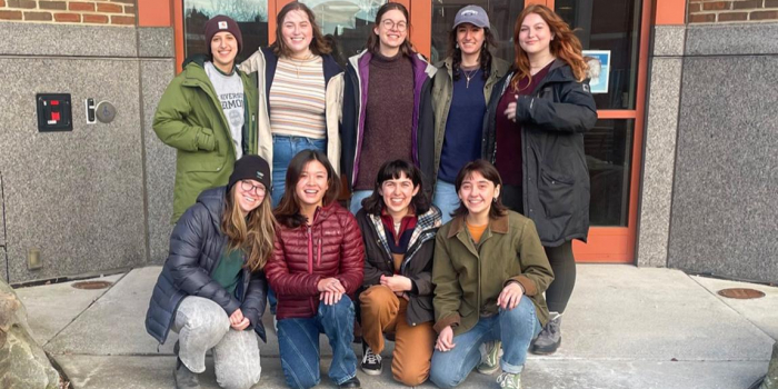 Eight female-identifying natural resource students pose in 2 rows in front of campus building