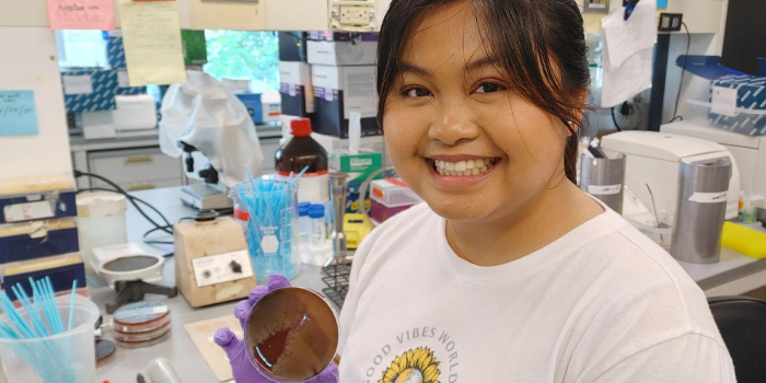 Graecia Pacheco in the Barlow Lab holding a plated bacteria specimen.