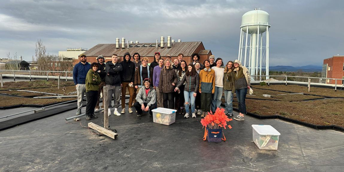 Group of 20 students stand on top of green roof overlooking view of University of Vermont campus.