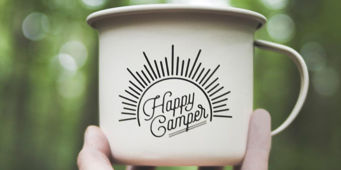 Hand holding a mug that says 'happy camper' on it