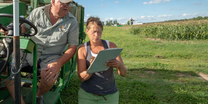 UVM Extension Professor and Agronomy Specialist Heather Darby talks to a man driving a tractor while working on a farm field.