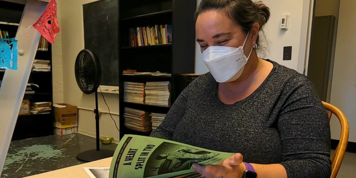 Teresa Mares sits at a desk in her office looking through Spanish comic books