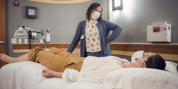 A patient lays in bed while a practitioner chats with her
