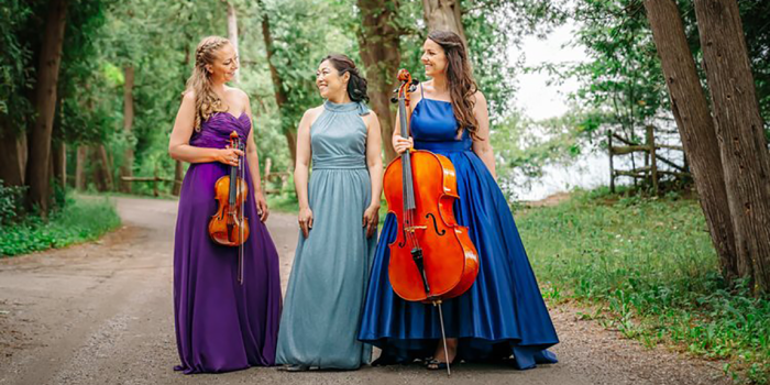 Ladies of the trio dressed to the nines on a dirt road with green trees in the backgroun