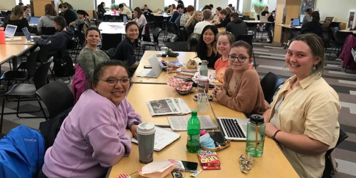 A group of college students sit in a cafeteria eating lunch