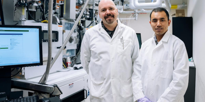Two scientists in white coats stand in a lab 
