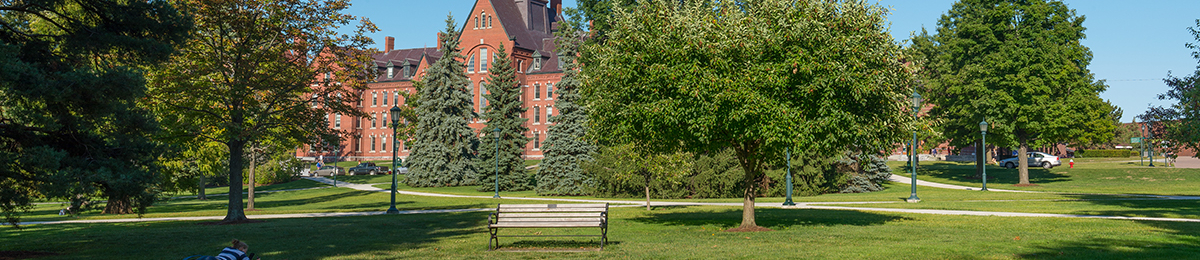UVM Green with trees leafed out. Old Mill in the background and a student in the grass in the foreground