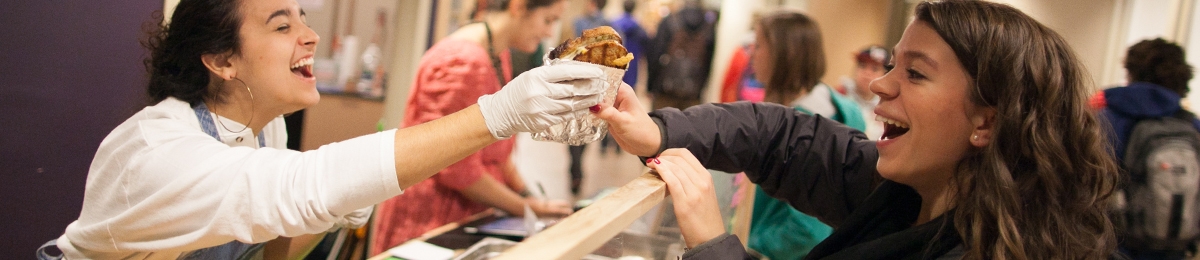 two students exchange a grilled cheese sandwich at the Feel Good stand