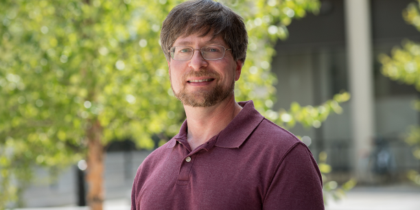 David Feurzeig smiling outdoors with campus greenery in the background