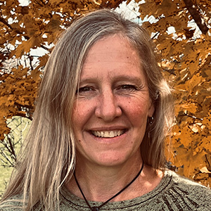 holly is smiling and standing in front of a maple tree with orange leaves