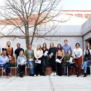 group of people gathered in front of a white building with a tree in the background