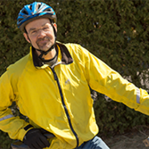 Richard Watts in a yellow jacket and bicycle helmet posing for the camera on his bike