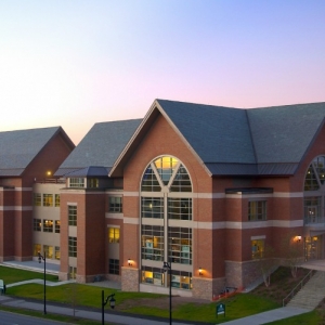 New brick building on campus, sky is purple with sun setting in background.