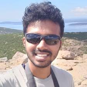 Headshot of Anoob Prakash on a mountaintop with sunglasses