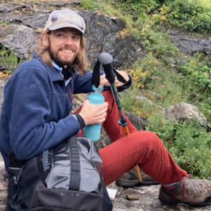 Dave taking a water break on a hike, sitting on a rock with hiking poles