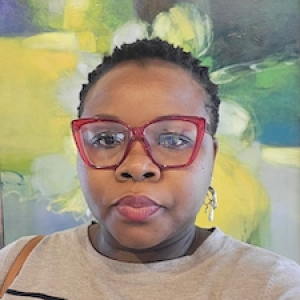Headshot of Sandra Nnadi with red glasses in front of a painting