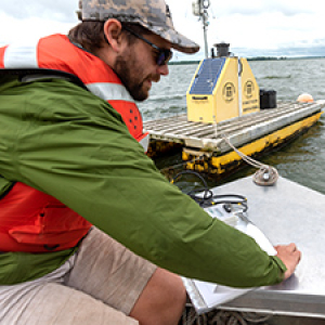 Researcher in orange life vest writes down observations on boat on lake near data buoy.