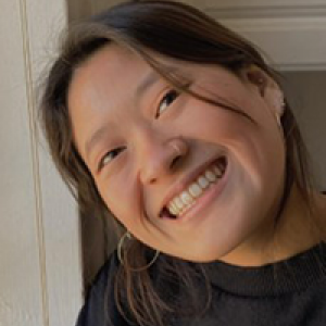 Kiki smiling with a head tilt standing next to a white wall