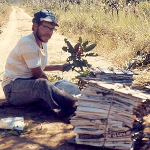 A young Dr. Hill sits by a dirt road, pressing stacks of specimens in newspapers 