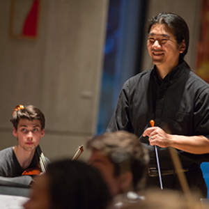 Professor Yutaka smiling with his orchestra students in the recital hall.