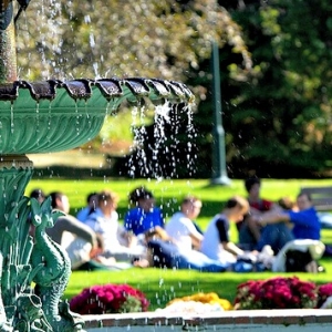 Water fountain on university green, students sitting around it.