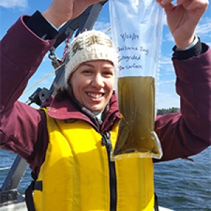 Student holds up water sample bag on boat on lake