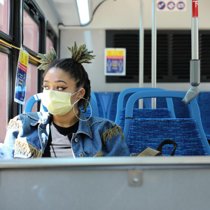  a person wearing a mask looks out the window while sitting inside a public bus