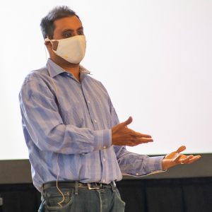 masked lecturer at podium