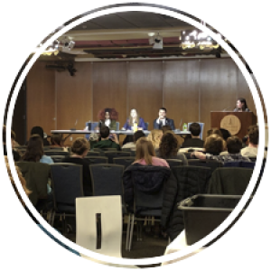 three students on a debate stage with a moderator and an audience watching them