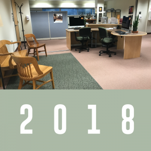 2018: Writing Centers Reception area with a large desk, computers, and chairs in front of a area rug with a wooden bench and chairs.