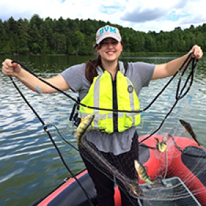 Graduate student in yellow life vest holds up net in red raft on a lake