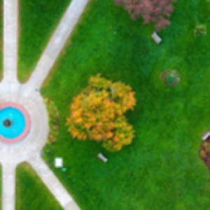 Aerial view of water fountain, lush green grass and sidewalks cutting through.