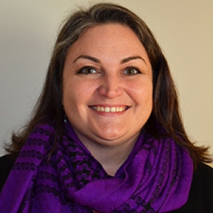 Molly is smiling at the camera, she has brown hair and wears a purple scarf.