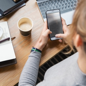 Person looking down at phone in front of them, at desk full of office supplies.