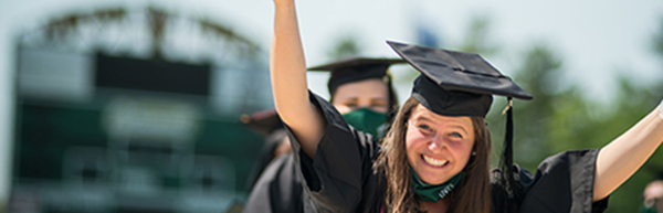 female student wearing regalia with arms up in celebration