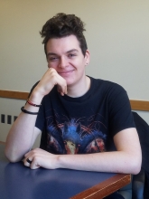 Seth Wade ('20) sitting at a table, smiling at camera resting chin in his right hand
