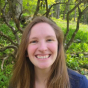 Chelsea Deraway: Middle aged Caucasian woman grinning and standing outside with a blue shirt and long light brown hair. 