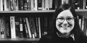 Black and white image of Devin smiling in a book lined room