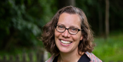 Caroline smiling broadly outdoors with trees and greenery in the background