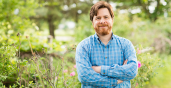 Peter Henne outdoors with wildflowers and trees in bloom behind him