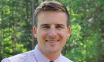 Alex smiling in shirt and tie against the greenery of Quechee, VT