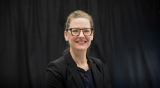 Pam smiling with hair pulled back with black velvet background