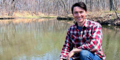 Be Tutko crouching by a small body of water