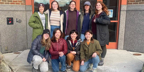 Eight female-identifying natural resource students pose in 2 rows in front of campus building