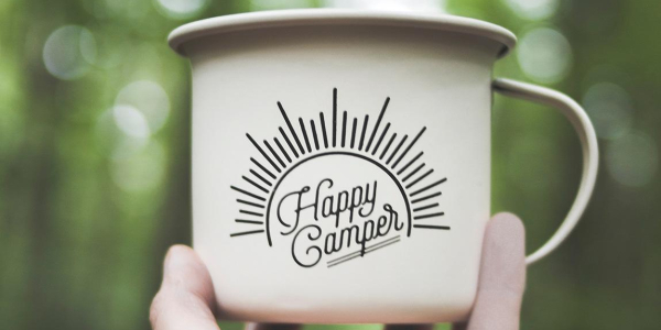 Hand holding a mug that says 'happy camper' on it