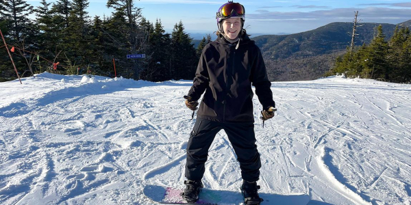 Katie Conlon stands on snowboard at top of ski resort trail.